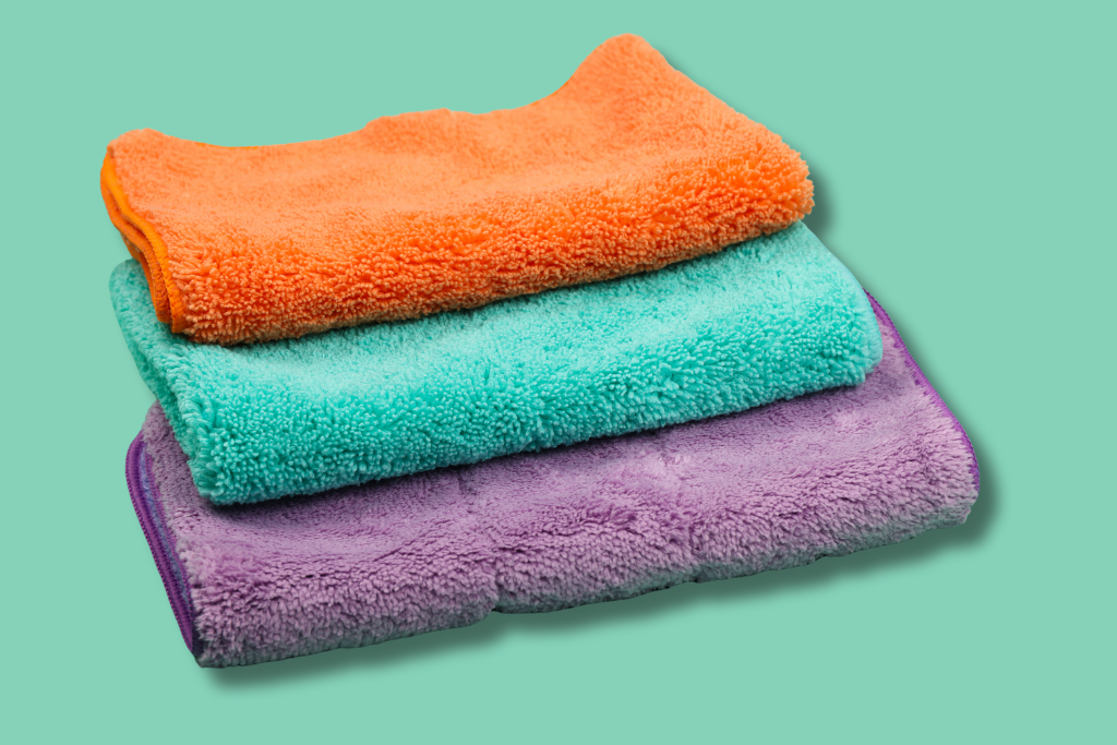 Stack of three colorful towels (orange, turquoise, purple) on a light green background